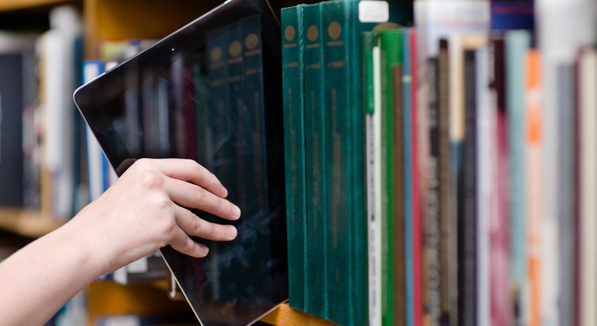 Hand nimmt ein Tablet aus einem Bücherregal